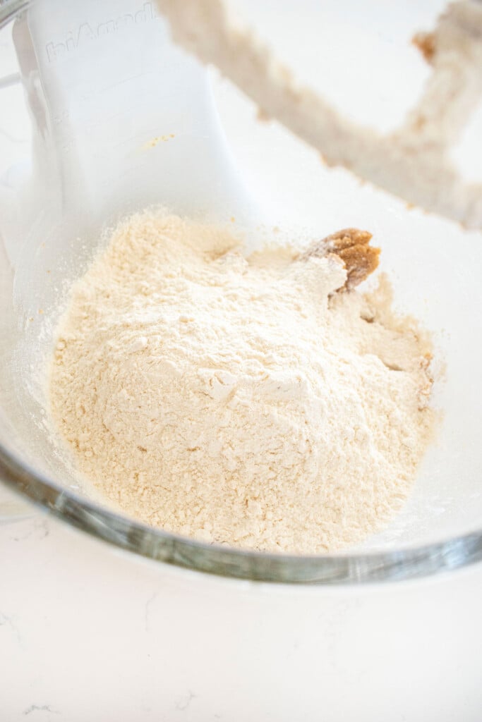 ingredients for maple caramel dark chocolate gingerbread cookie dough in a glass mixing bowl on a white marble counter.