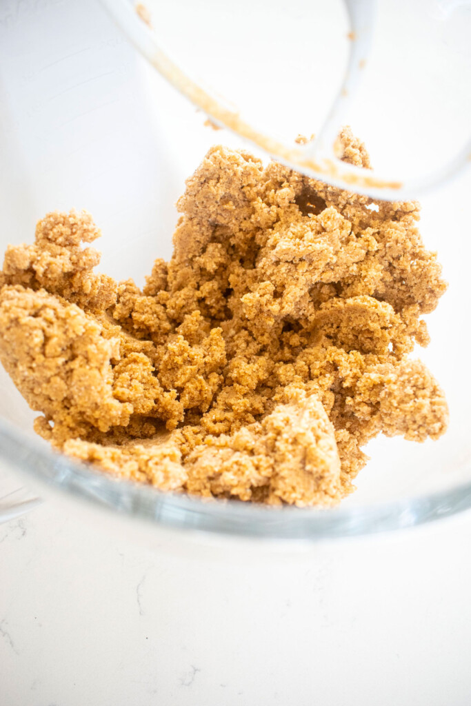 maple caramel dark chocolate gingerbread cookie dough in a glass mixing bowl on a white marble counter.