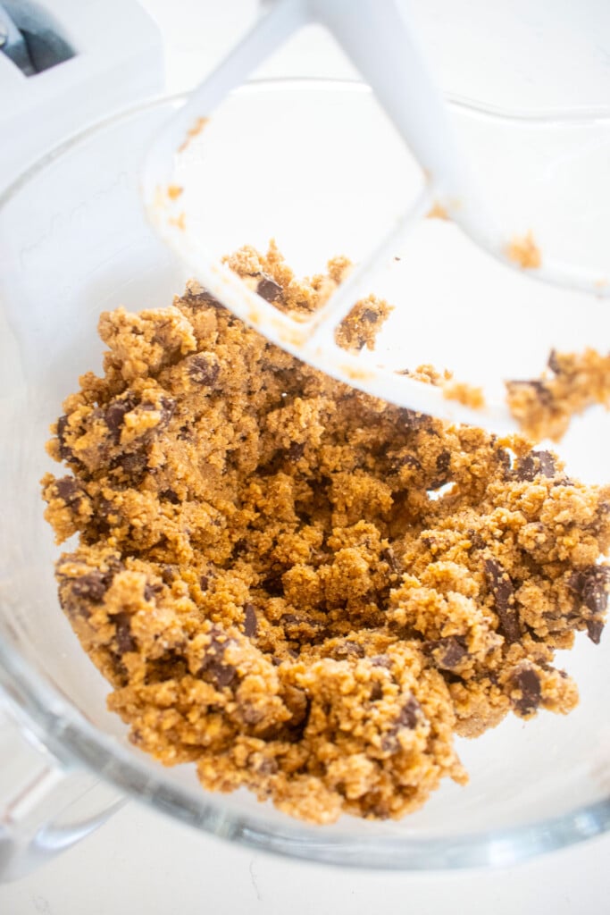 maple caramel dark chocolate gingerbread cookie dough in a glass mixing bowl on a white marble counter.