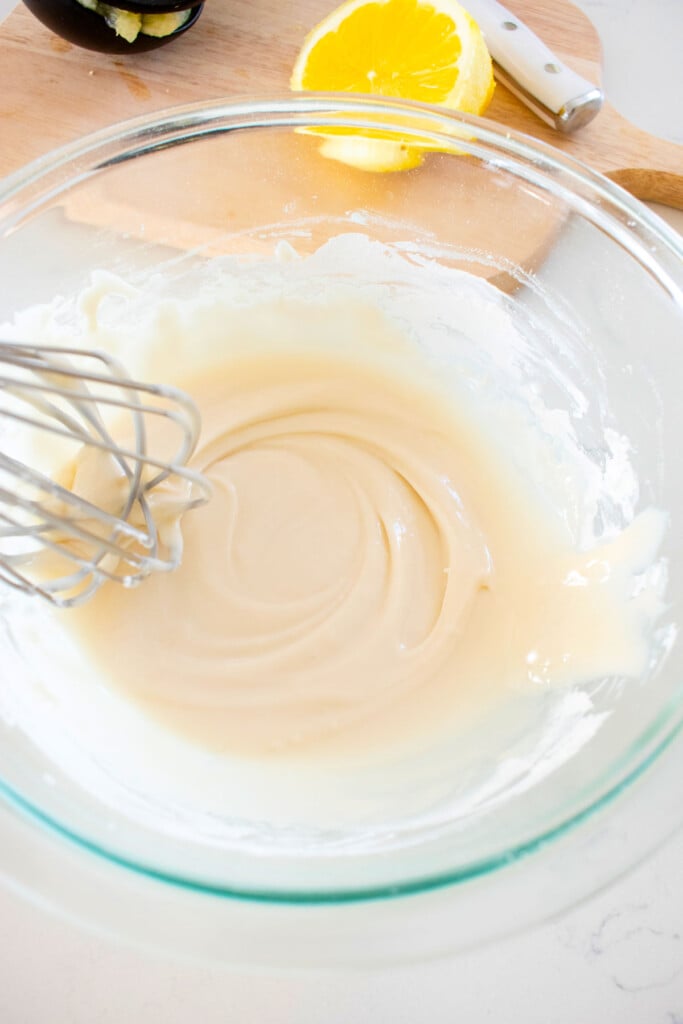 meyer lemon glaze in a glass mixing bowl being whisked on a white marble counter.