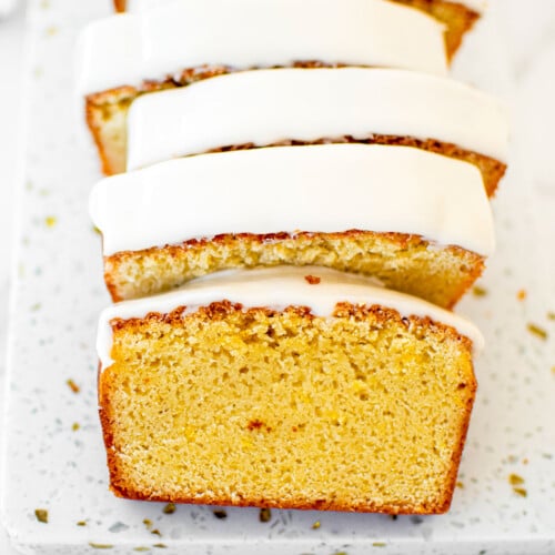 meyer lemon pound cake loaf sliced into slices on a white marble cutting board.