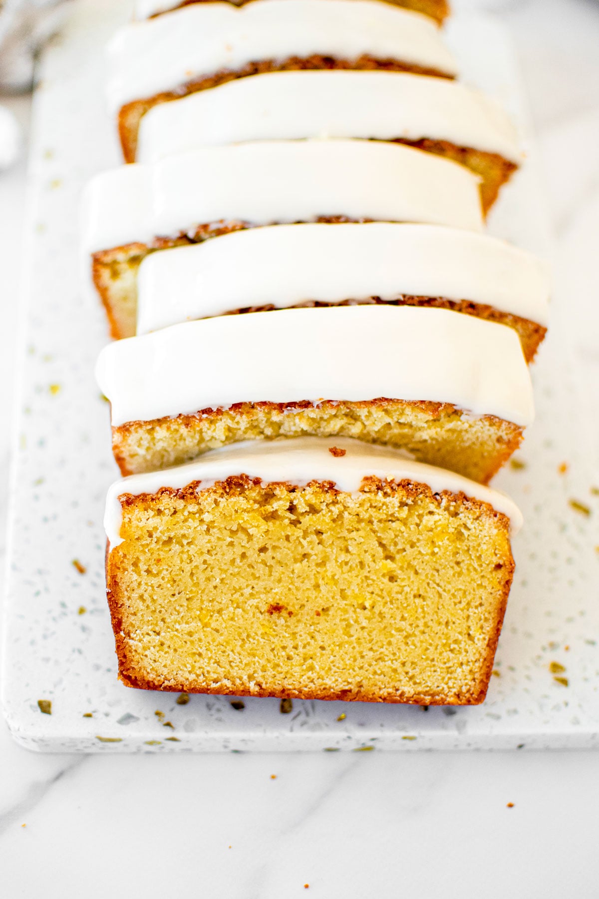meyer lemon pound cake loaf sliced into slices on a white marble cutting board.
