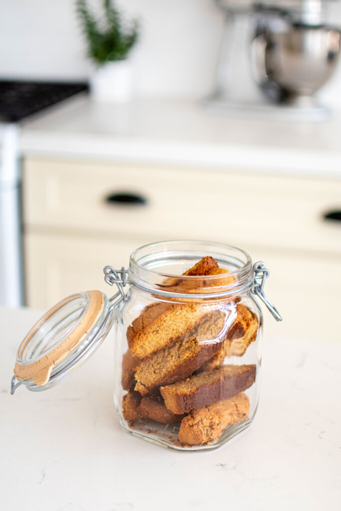 peanut butter biscotti for dogs in a glass cookie jar on a white marble kitchen countertop.