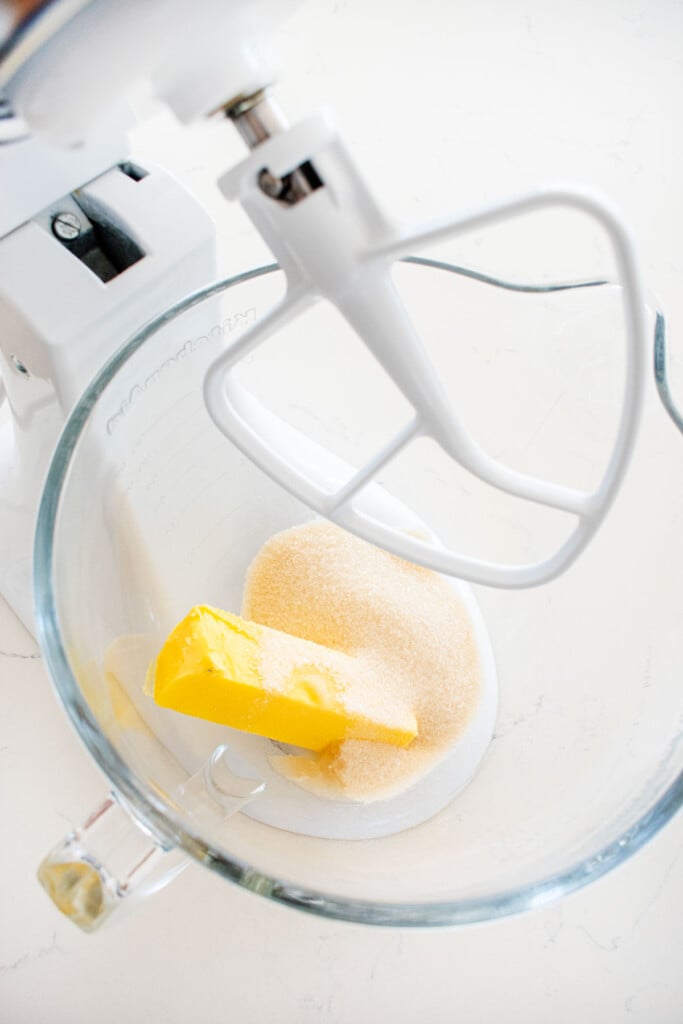 butter sugar and peppermint extract in a glass mixing bowl on a white marble counter.