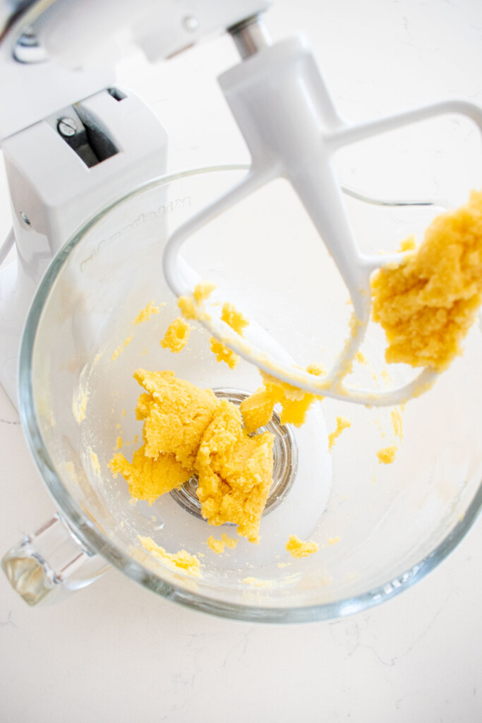 creamed butter and sugar in a glass mixing bowl on a white marble counter.