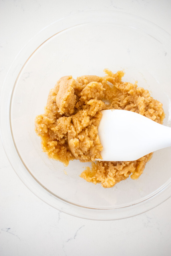 streusel topping being made in a glass mixing bowl with a spatula on a white marble counter.