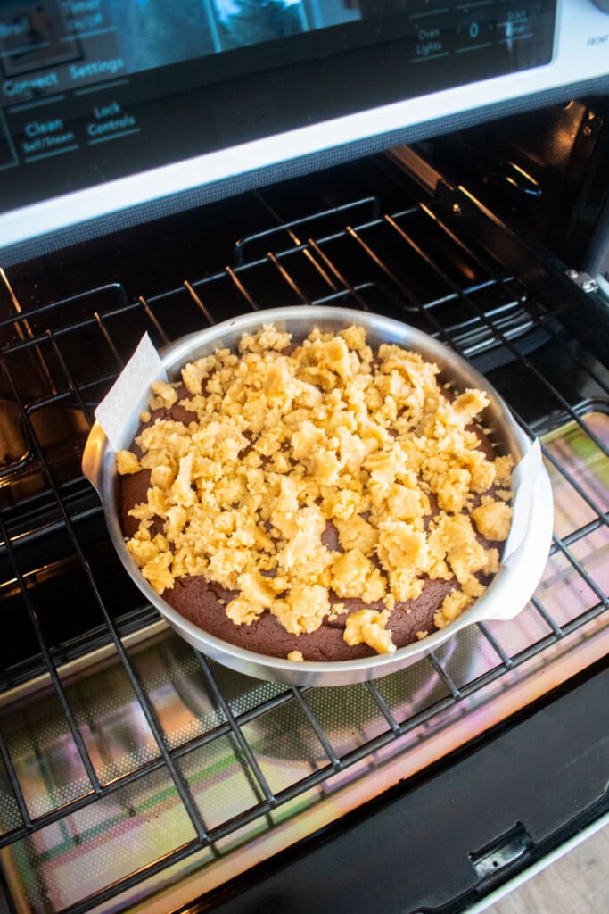 streusel topping being added on top of a partially baked peppermint mocha coffee cake in the oven.
