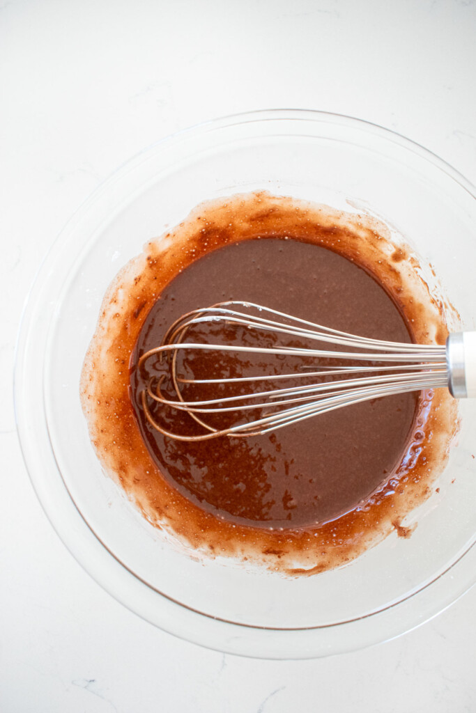 chocolate espresso glaze with a whisk in a glass mixing bowl on a white marble counter.