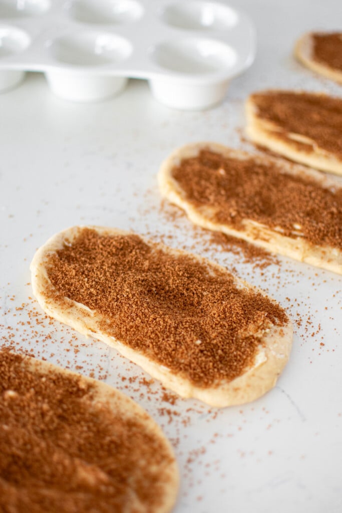 spiced eggnog babka buns dough spread with butter and topped with brown sugar on a white marble counter.