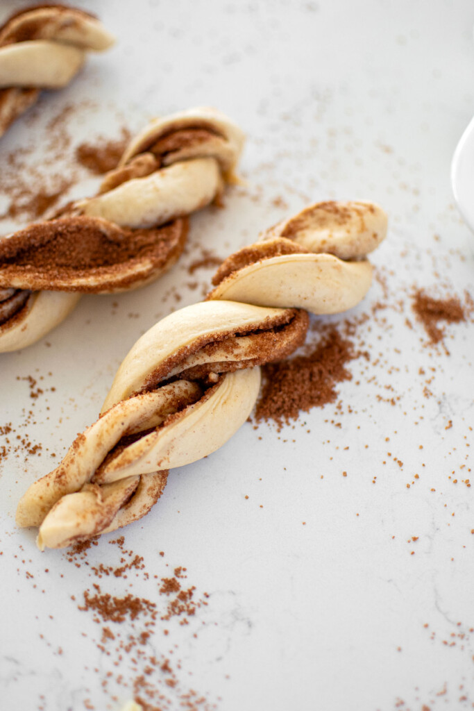spiced eggnog babka buns rolled into logs and cut down the middle and twisted on a white marble counter.