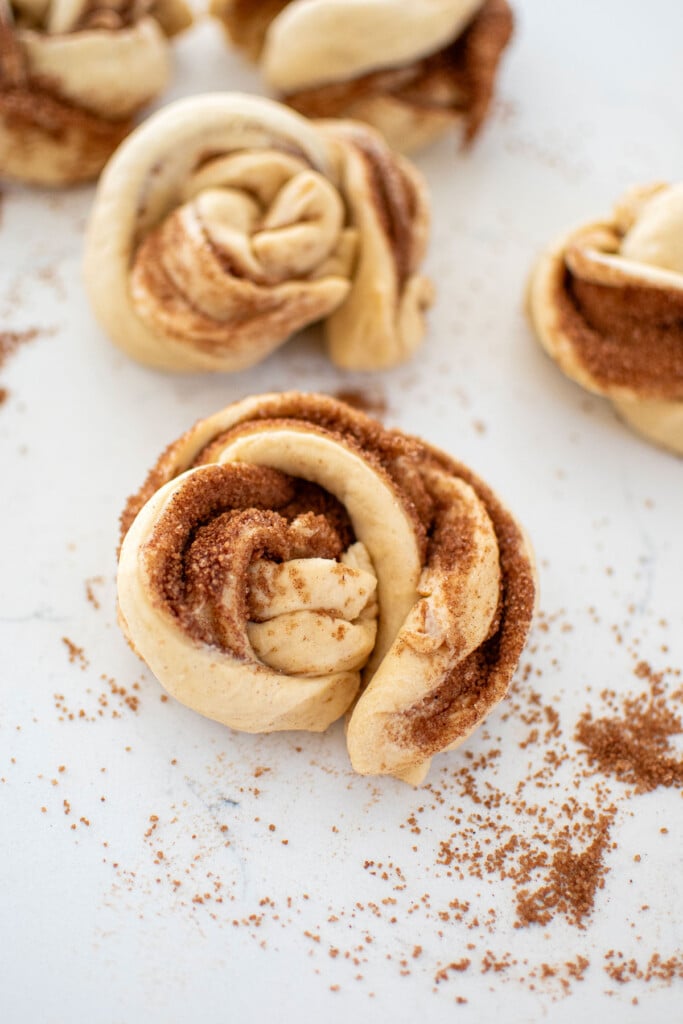 spiced eggnog babka buns rolled into logs and cut down the middle and twisted into a spiral bun on a white marble counter.