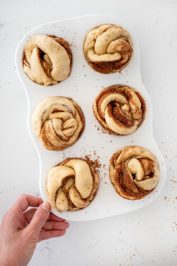 raw spiced eggnog babka buns in a white muffin pan on a marble counter.
