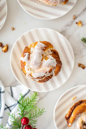 spiced eggnog babka buns with glaze on small stripe dessert plates on a marble counter.