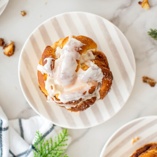 spiced eggnog babka buns with glaze on small stripe dessert plates on a marble counter.