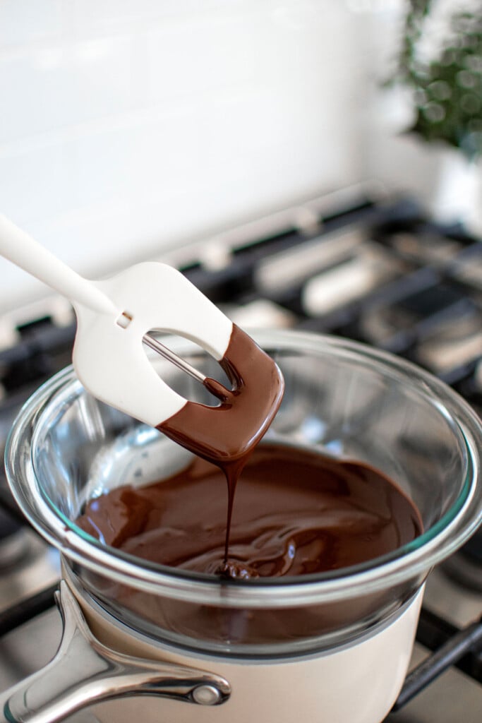 melted dark chocolate in a double boiler on the stove with a candy thermometer in it.