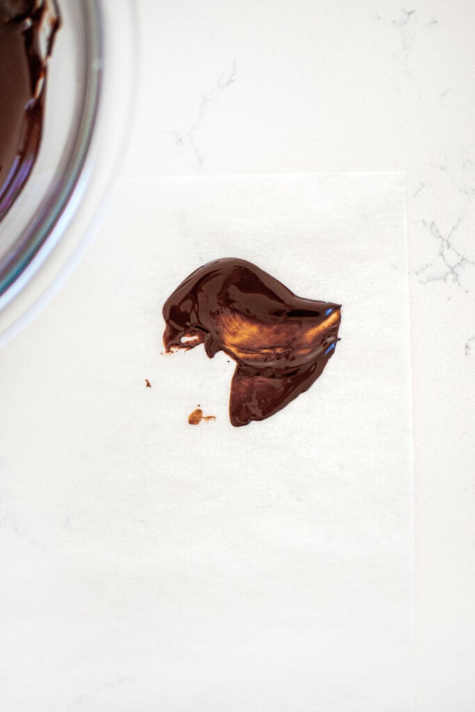 piece of white parchment paper with a small bit of chocolate on it on a white marble counter.