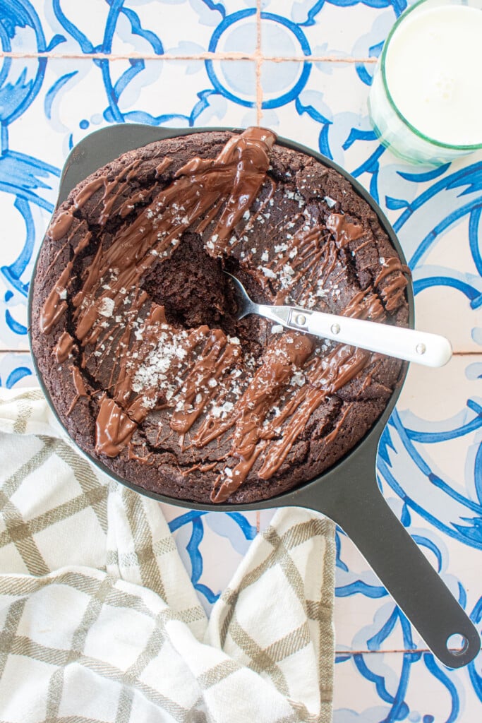 bone broth brownies in a cast iron skillet with a spoon in the middle on a blue tile table.