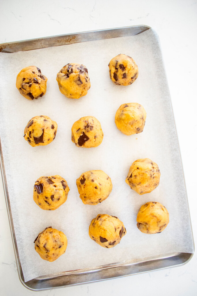 brown butter caramel dark chocolate cookie dough balls on a baking sheet on a marble counter.