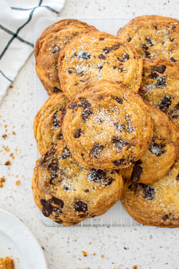brown butter caramel dark chocolate cookies with sea salt on a cooling rack on a marble counter.