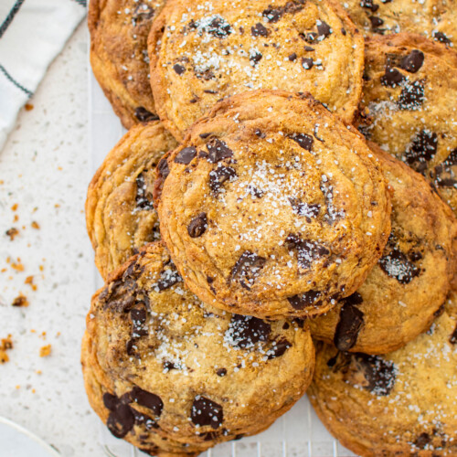 brown butter caramel dark chocolate cookies with sea salt on a cooling rack on a marble counter.