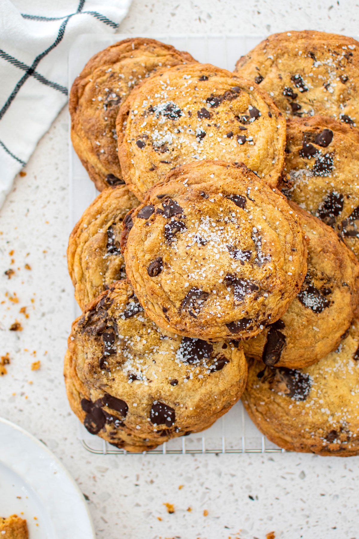 brown butter caramel dark chocolate cookies with sea salt on a cooling rack on a marble counter.