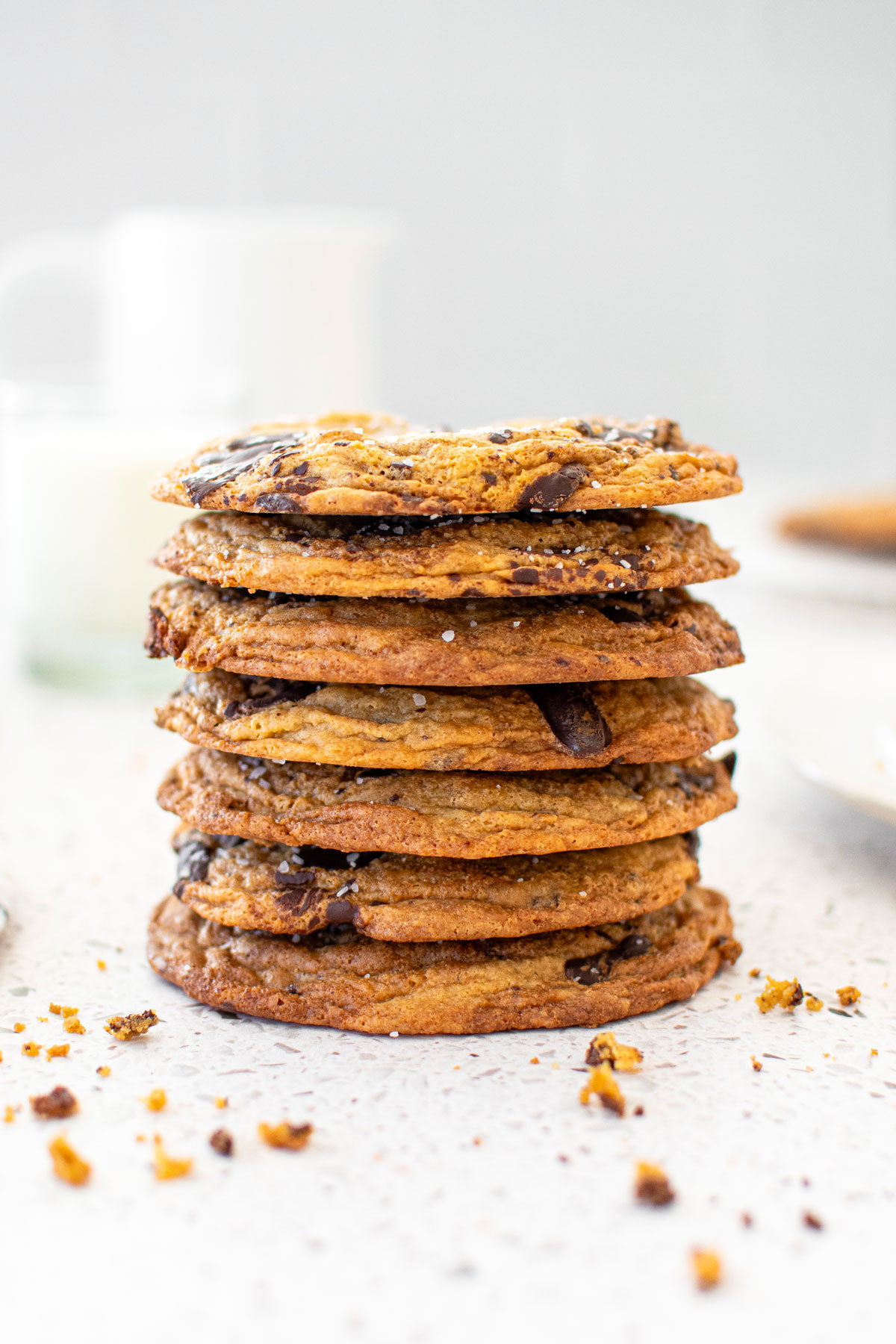 stack of brown butter caramel dark chocolate cookies on a marble counter with a glass of milk.