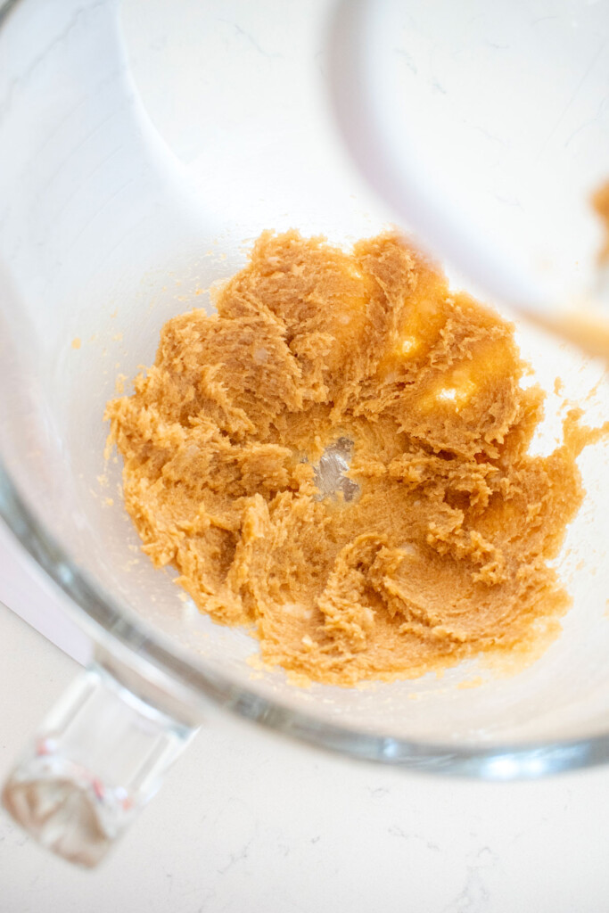 creamed coconut oil and brown sugar in a glass mixing bowl on a marble counter.