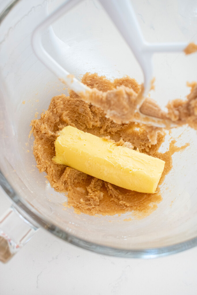 creamed brown sugar and coconut oil with a stick of butter in a glass mixing bowl on a marble counter.