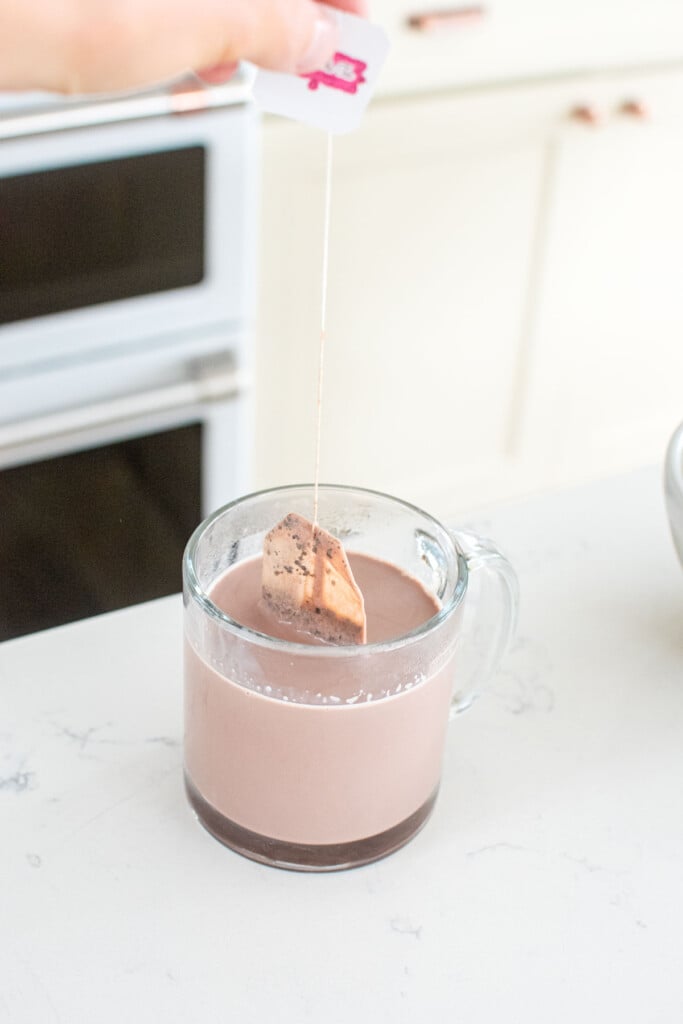 a chai tea bag being steeped in a mug of hot chocolate on the kitchen counter.
