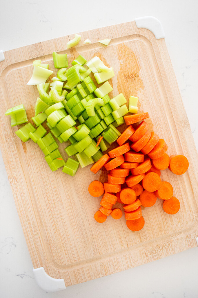 cut carrots and celery on a wood cutting board on a white marble counter.