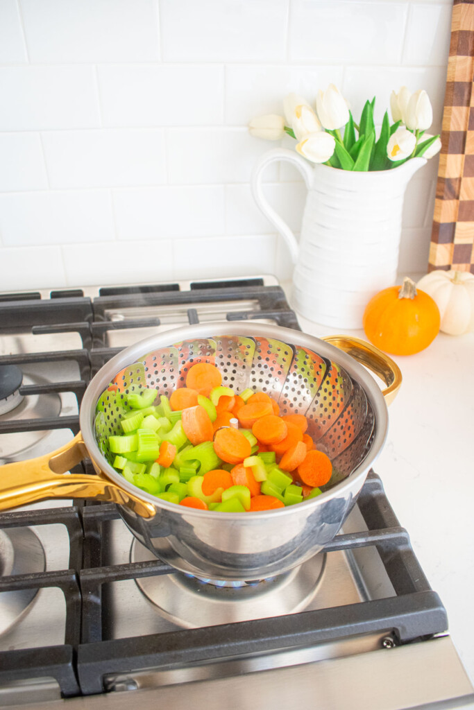 sliced carrots and celery in a steaming basket in a small pot on the stovetop.