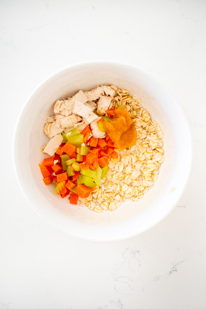 chicken and pumpkin dinner for dogs being made in a white dog bowl on a marble counter.