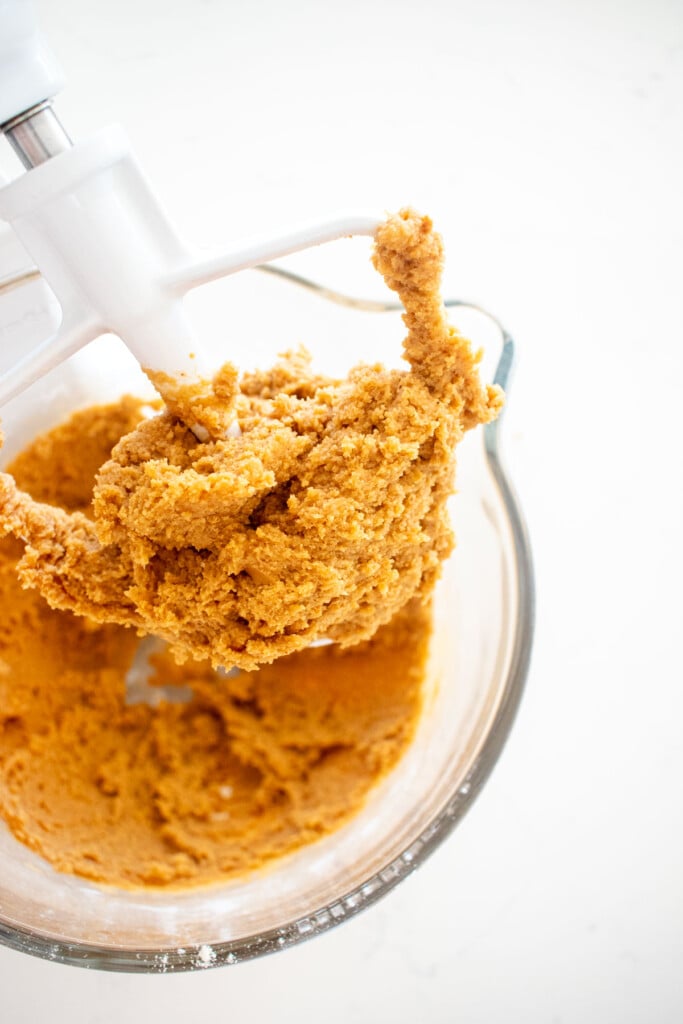 eggless peanut butter cookie dough in a glass stand mixing bowl on a white marble counter.