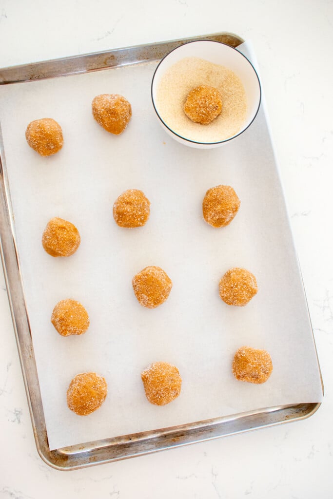 eggless peanut butter cookie dough balls rolled in cane sugar on a baking sheet on a marble counter.