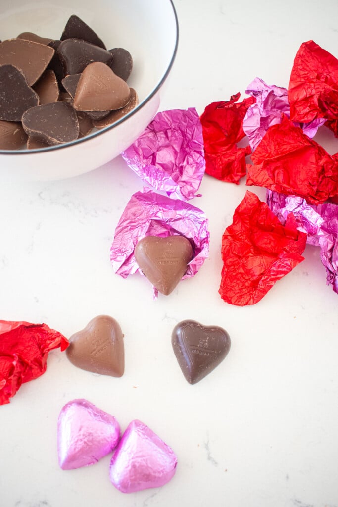 chocolate hearts in pink and red foil being unwrapped on a marble counter.