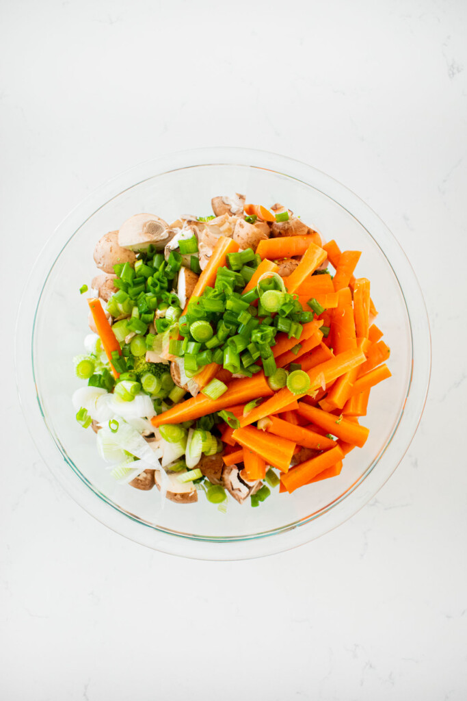 mixed veggies in a glass mixing bowl on a white marble counter.