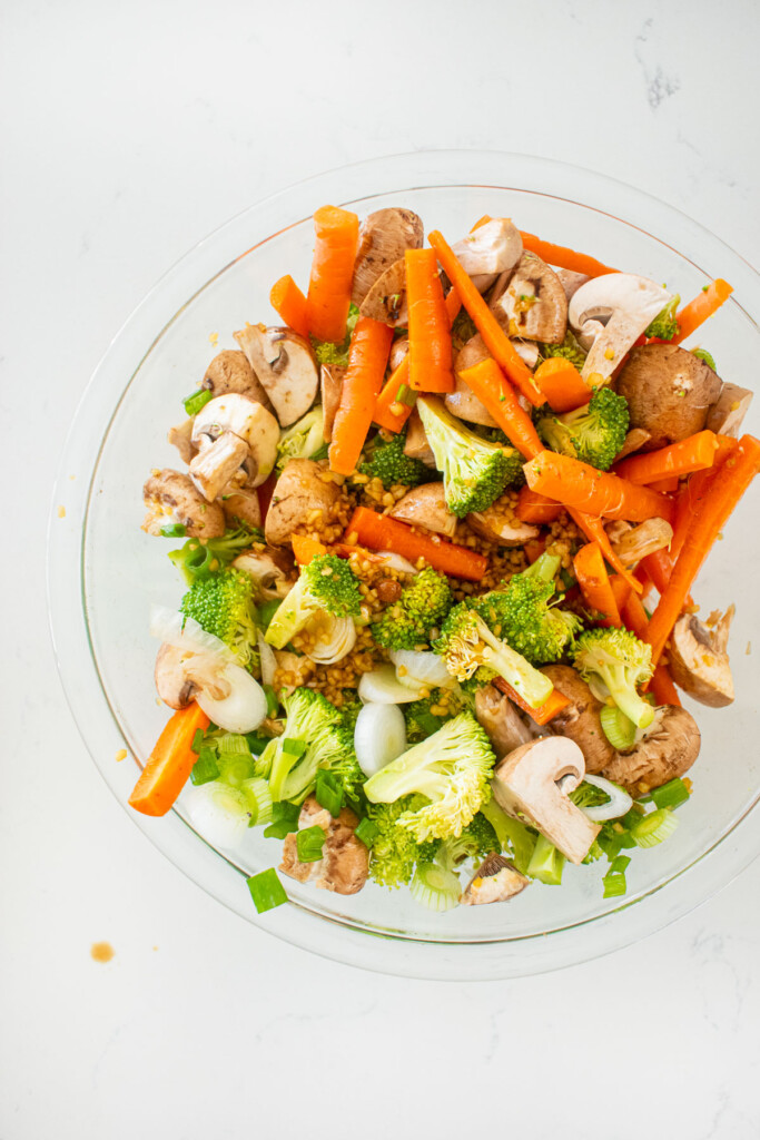 bowl of veggies with honey garlic glaze in a glass mixing bowl on a white marble counter.