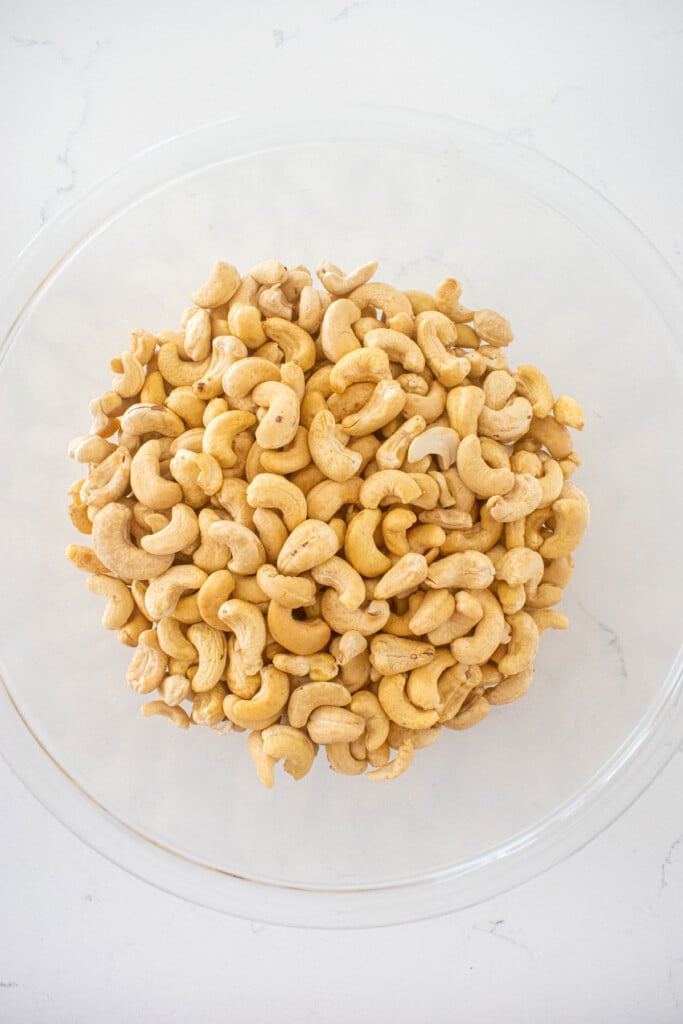 raw cashews in a glass mixing bowl on a white marble countertop.