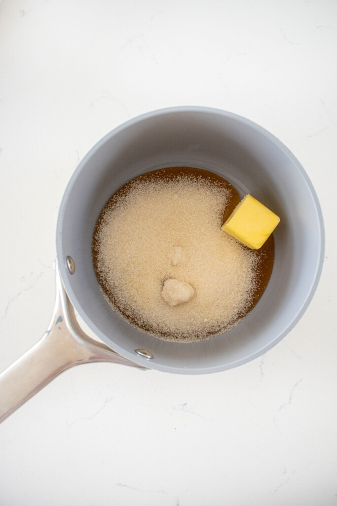 honey, sugar and butter in a small pot on a white marble countertop.