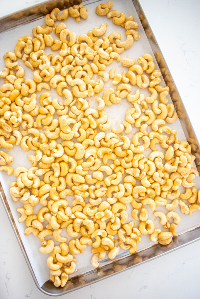 raw honey cashews on a baking sheet on a white marble countertop.