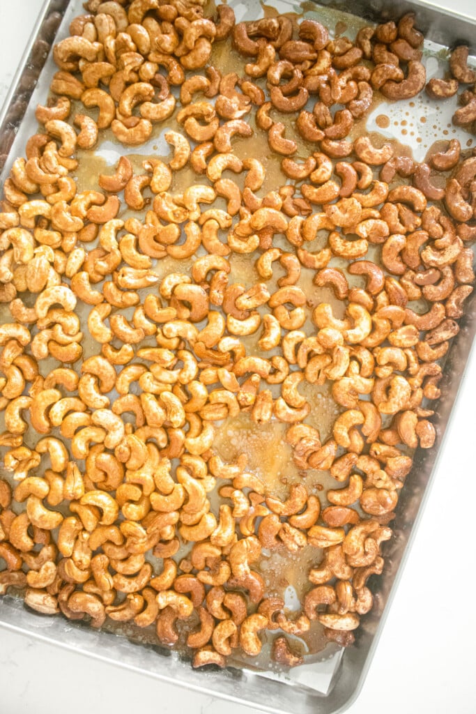 honey roasted cashews on a baking sheet on a white marble countertop.