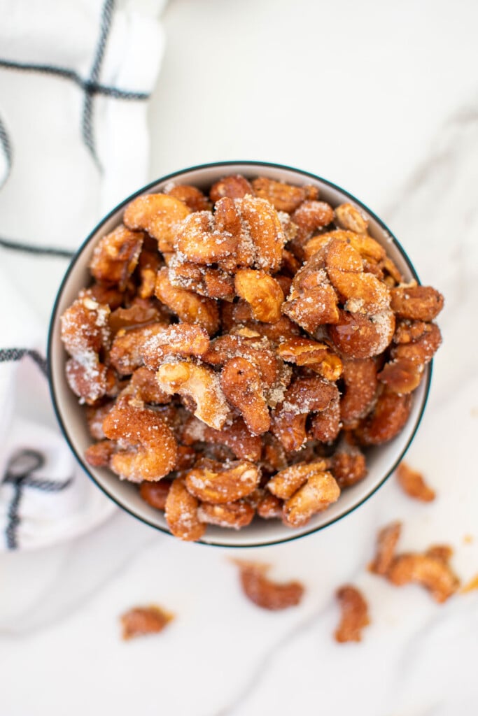honey roasted cashews in a bowl on a white marble countertop.