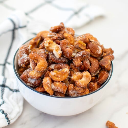 honey roasted cashews in a bowl on a white marble countertop.