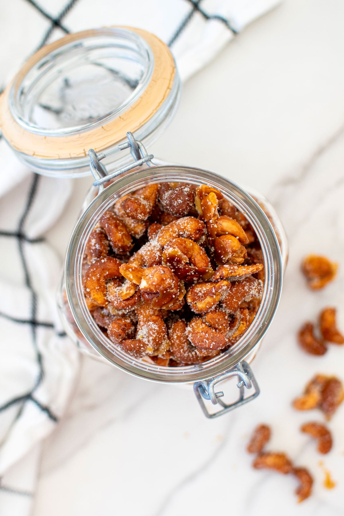 honey roasted cashews in a glass canister on a white marble countertop.