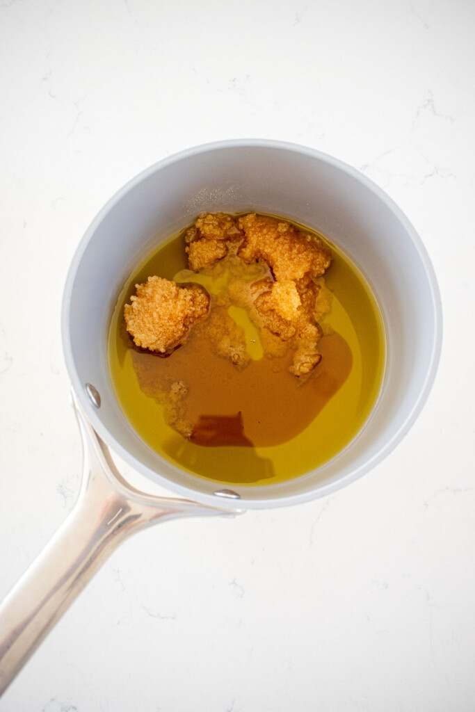 honey, olive oil and maple syrup in a small pot on a white marble countertop.