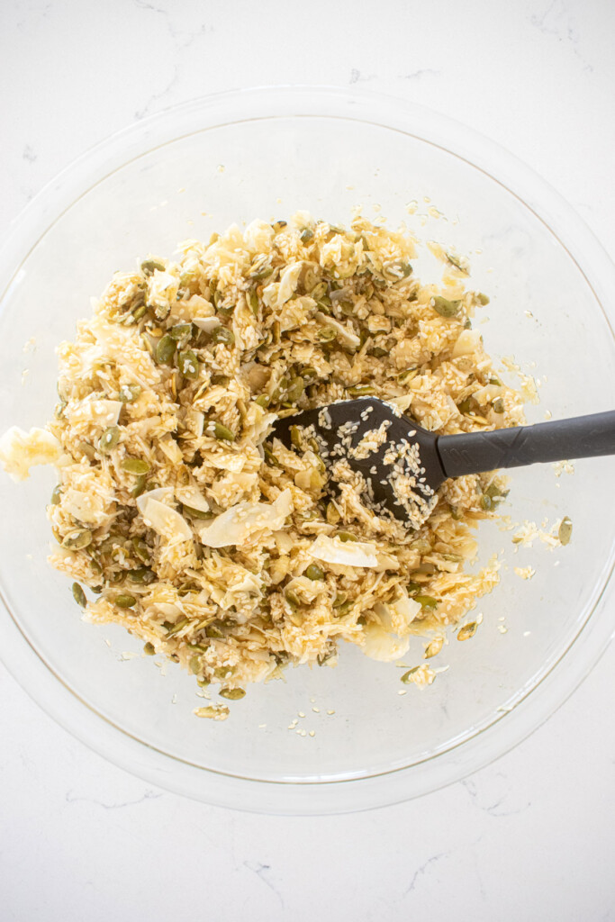 honey sesame dark chocolate bark ingredients being mixed together in a glass mixing bowl on a white marble countertop.