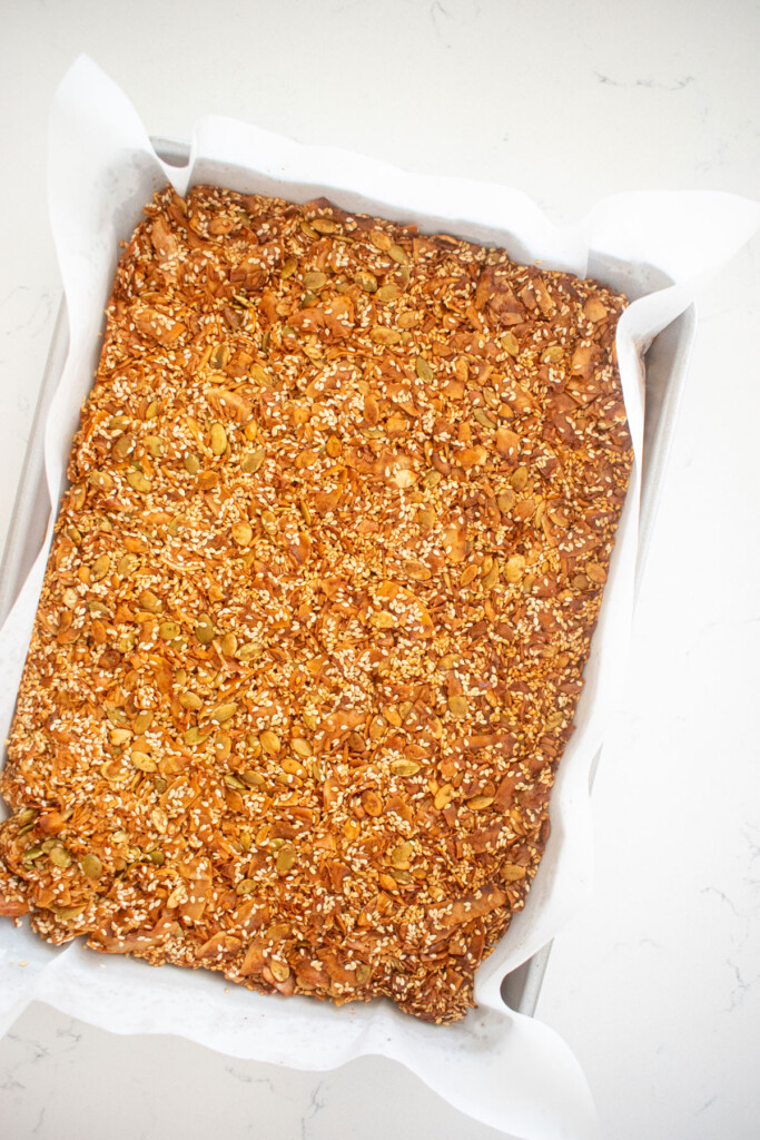 baked honey sesame dark chocolate bark on a a baking sheet on a white marble countertop.