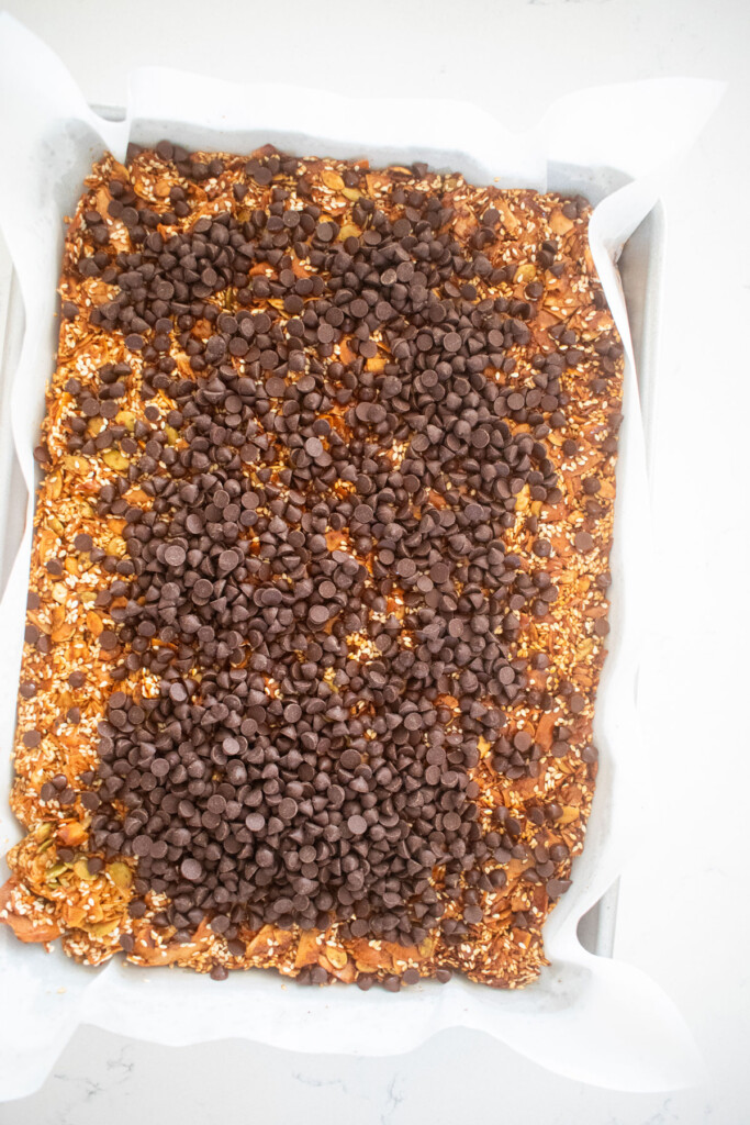 baked honey sesame dark chocolate bark with chocolate chips melting on top of the baking sheet on a marble countertop.