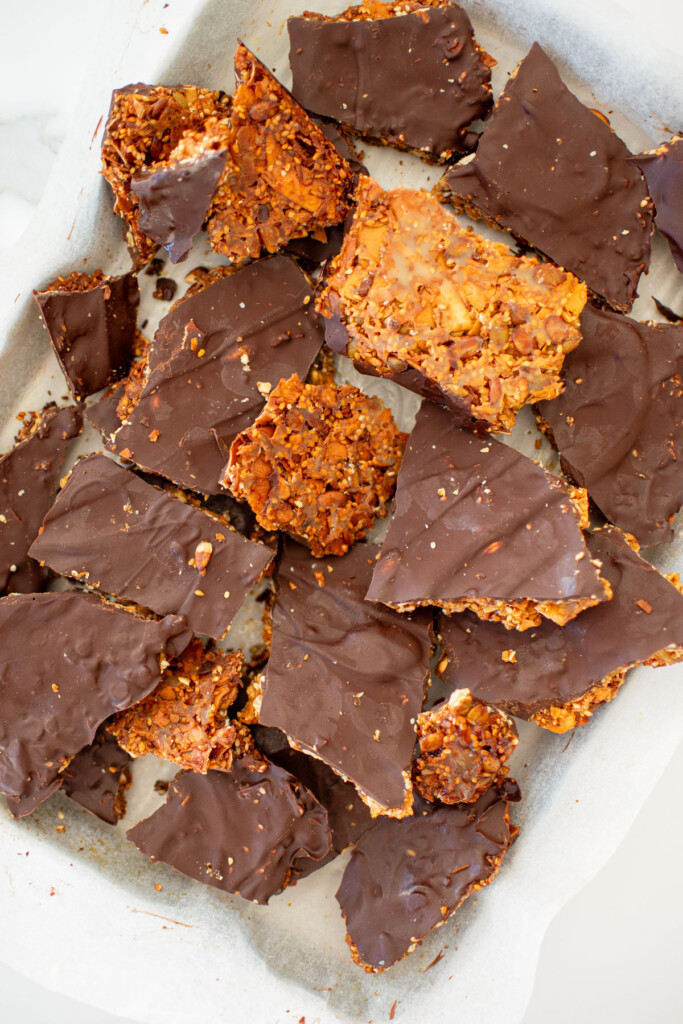 honey sesame dark chocolate bark broken into pieces on a baking sheet.
