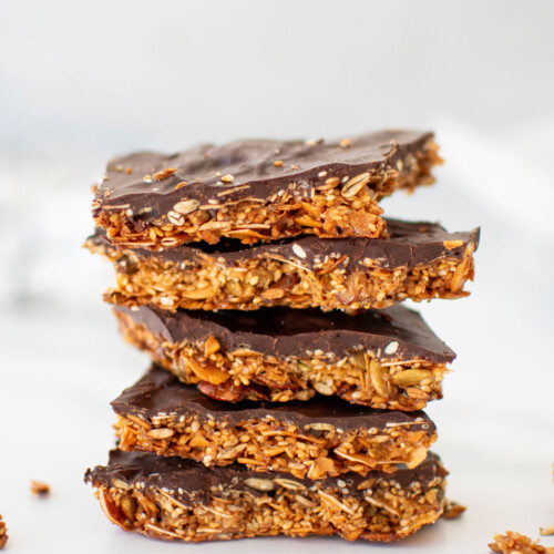 honey sesame dark chocolate bark pieces stacked on a white marble countertop.